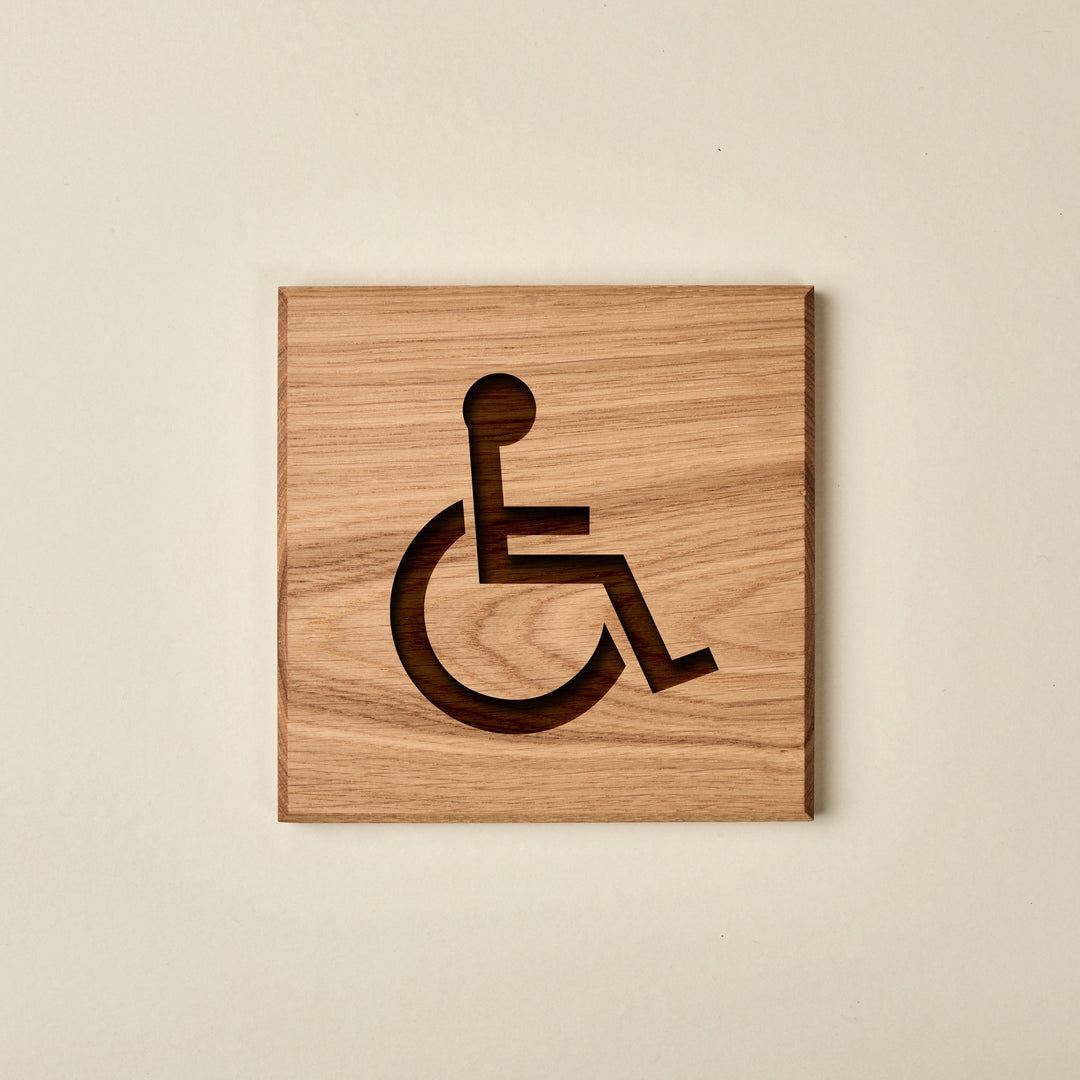 Square oak wood accessibility sign with a engraved wheelchair symbol. The sign features a warm, natural wood finish and a horizontal grain pattern.
