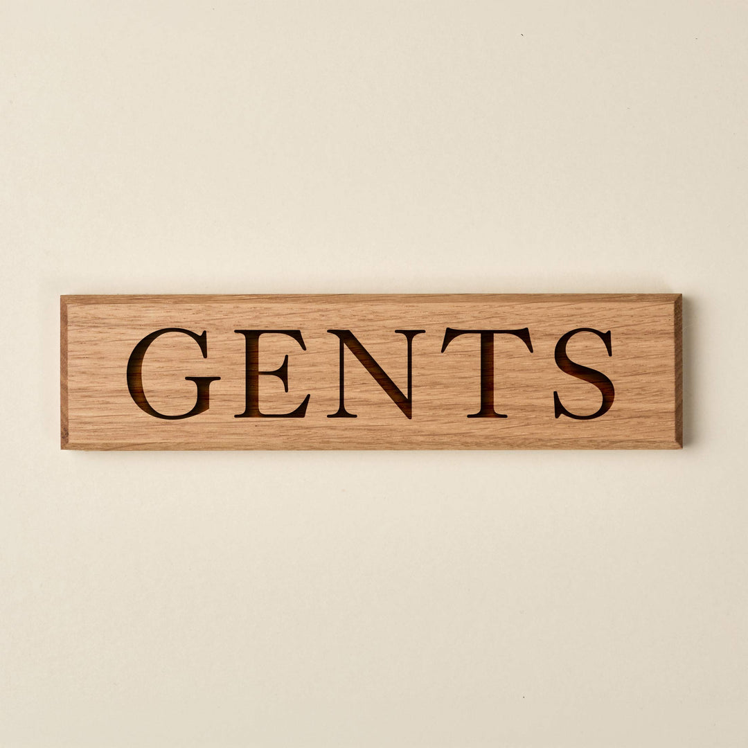 Horizontal oak "GENTS" door sign featuring engraved serif lettering. The sign showcases a warm, natural wood finish with a visible grain and dark recessed text.