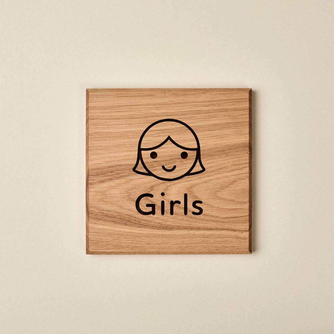 Square Oak children’s toilet sign featuring a simple, smiling girl illustration and the engraved text "Girls" in a rounded typeface.