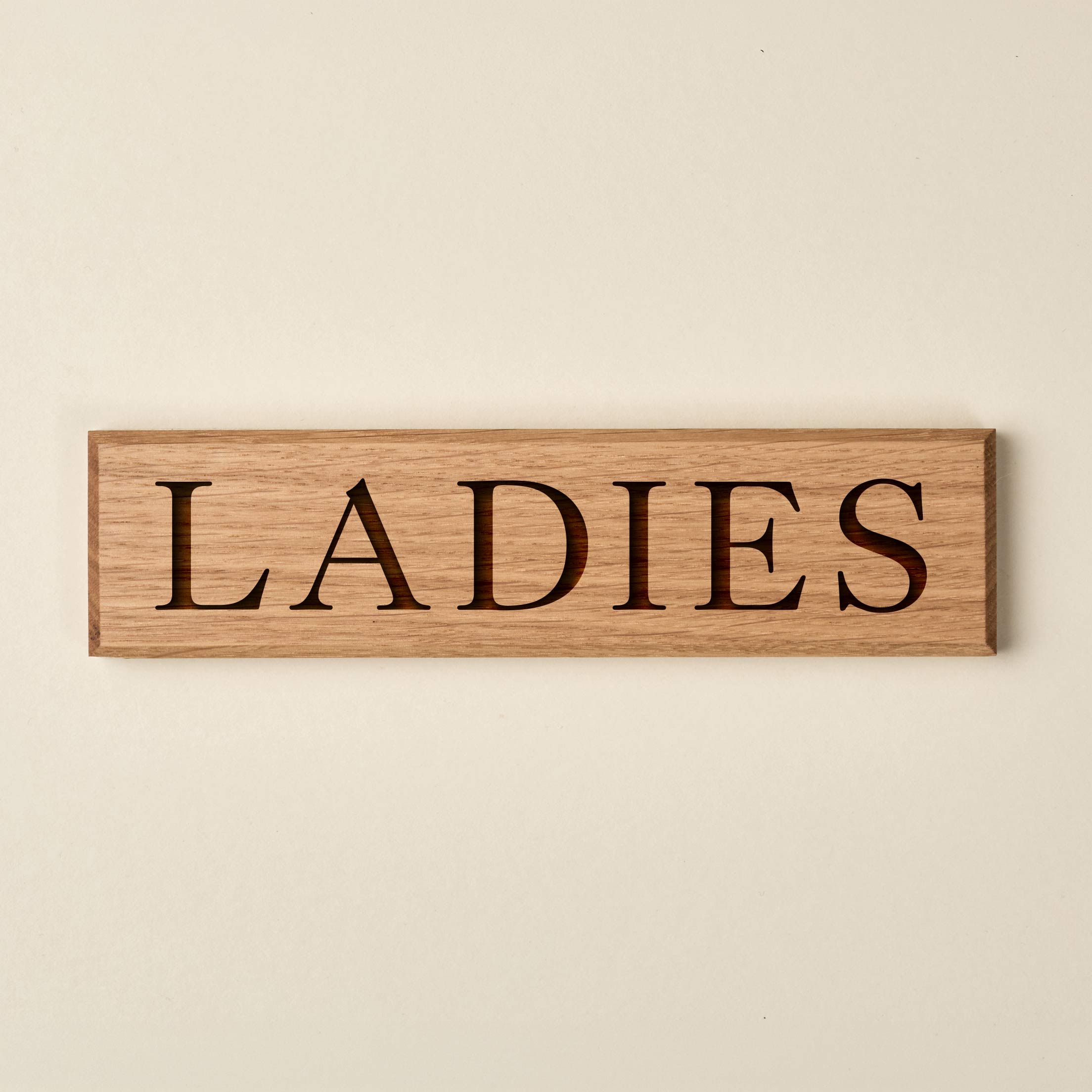 Horizontal oak "LADIES" door sign featuring engraved serif lettering. The sign showcases a warm, natural wood finish with a visible grain and dark recessed text.