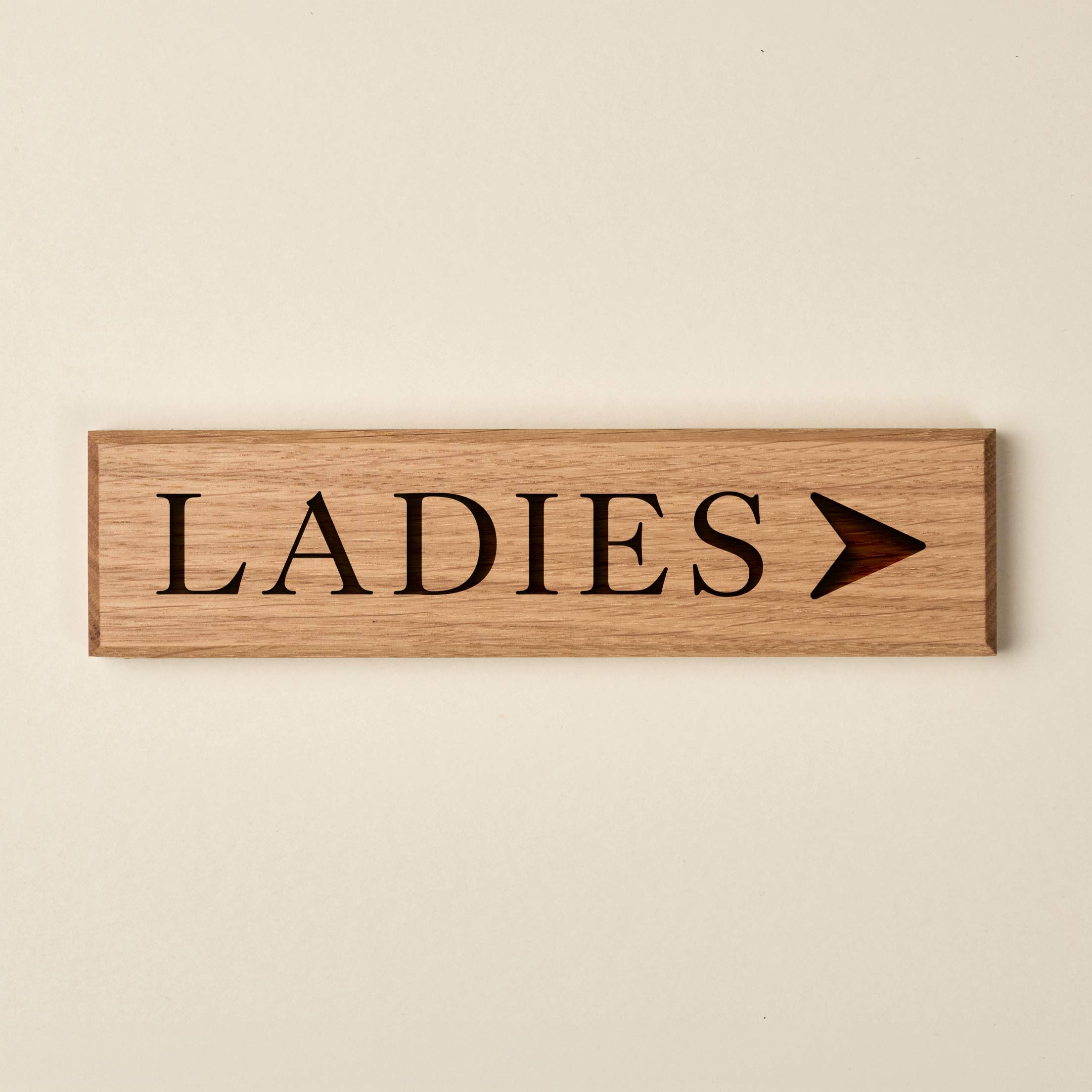 Slimline oak "LADIES" directional sign featuring engraved serif lettering and a right-pointing arrow. The natural wood finish has a visible horizontal grain and dark recessed text.