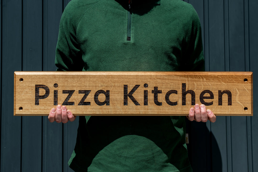 Oak Sign engraved with Pizza Kitchen, held in two hands upright. 