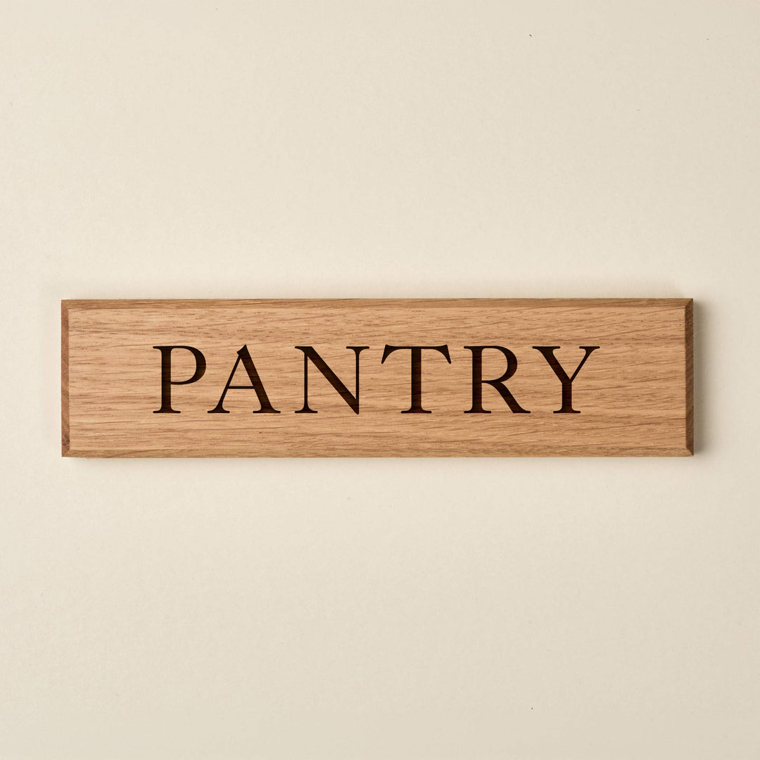 A rectangular oak wood door sign with the word "PANTRY" engraved into the surface in a classic serif font.