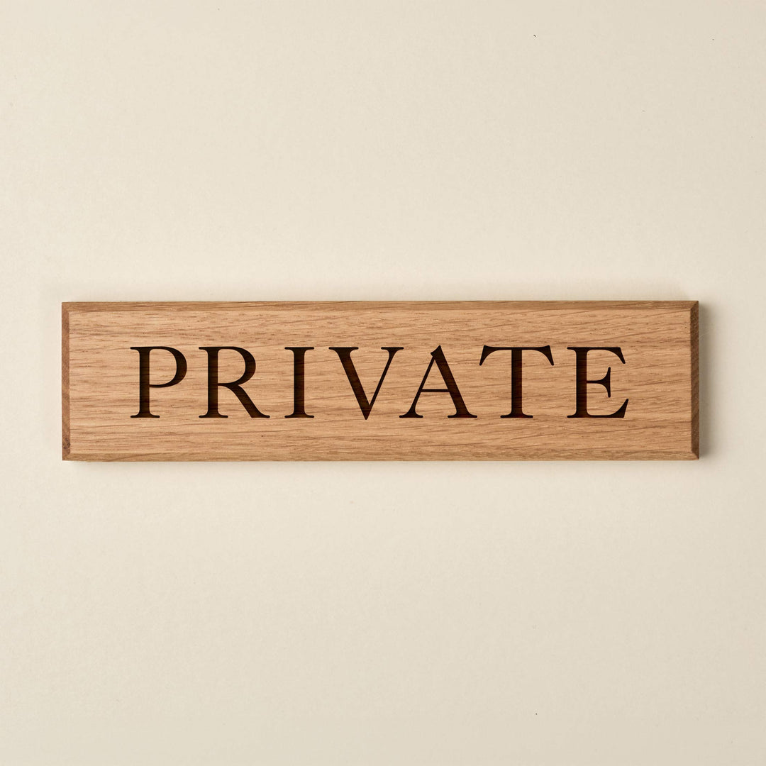 A rectangular oak wood door sign with the word "PRIVATE" engraved into the surface in a serif font.