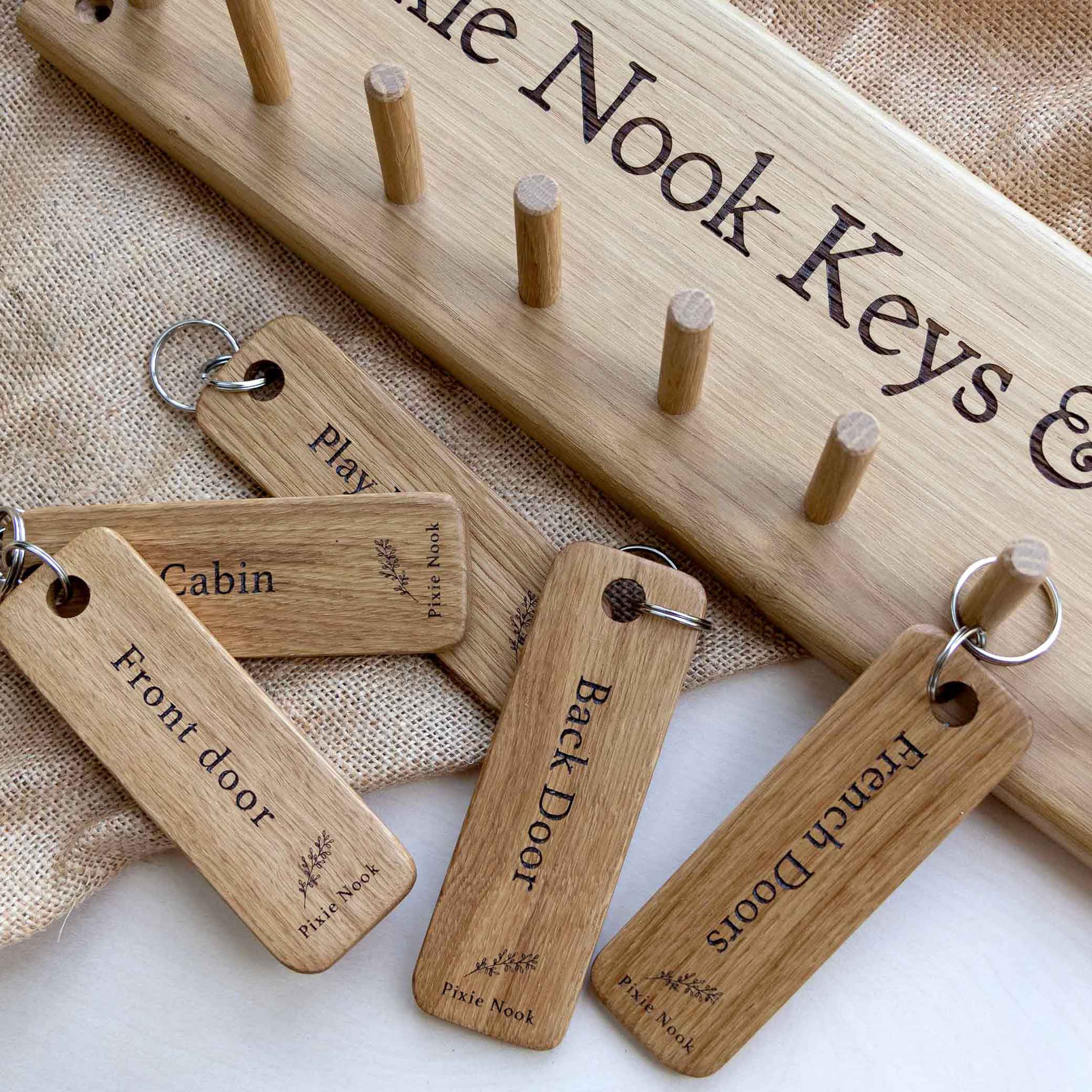 Oak Rack with Shaker Pegs engraved with Pixie Nook Keys, with 5 Oak engraved key fobs.  Lying flat on a hessian and plain background