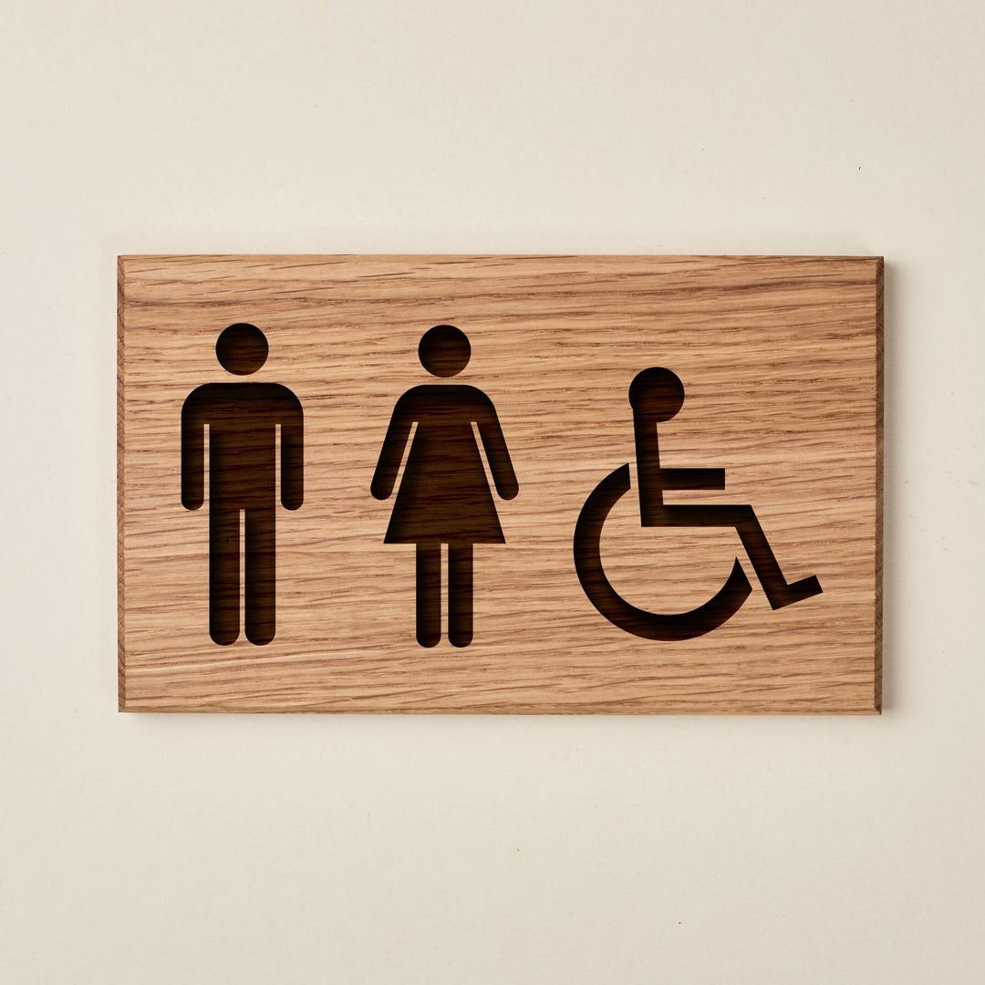 rectangular oak restroom sign with engravedsymbols for men, women, and wheelchair accessibility. The natural wood grain runs horizontally across the entire plaque.