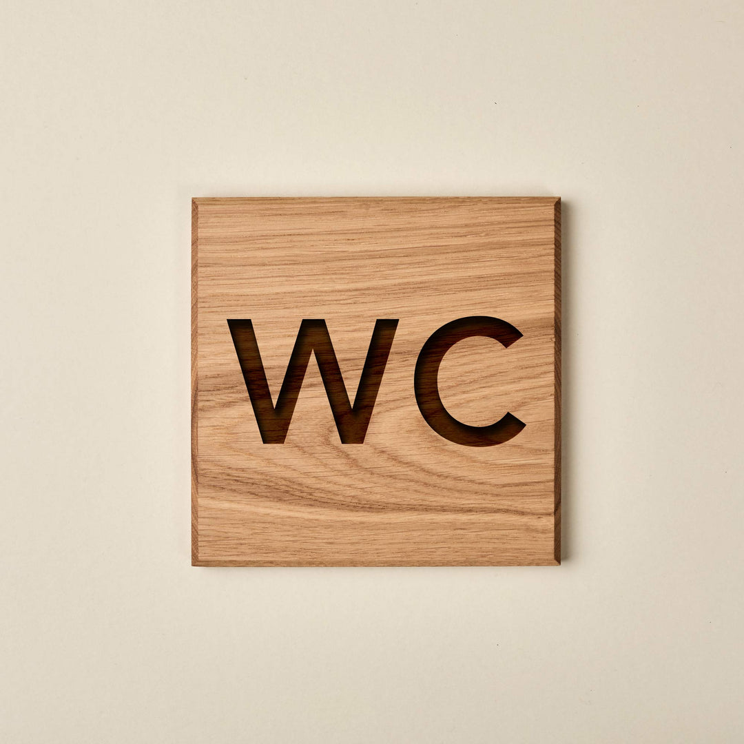 Square oak restroom sign featuring engraved "WC" lettering with a dark, recessed wood finish.
