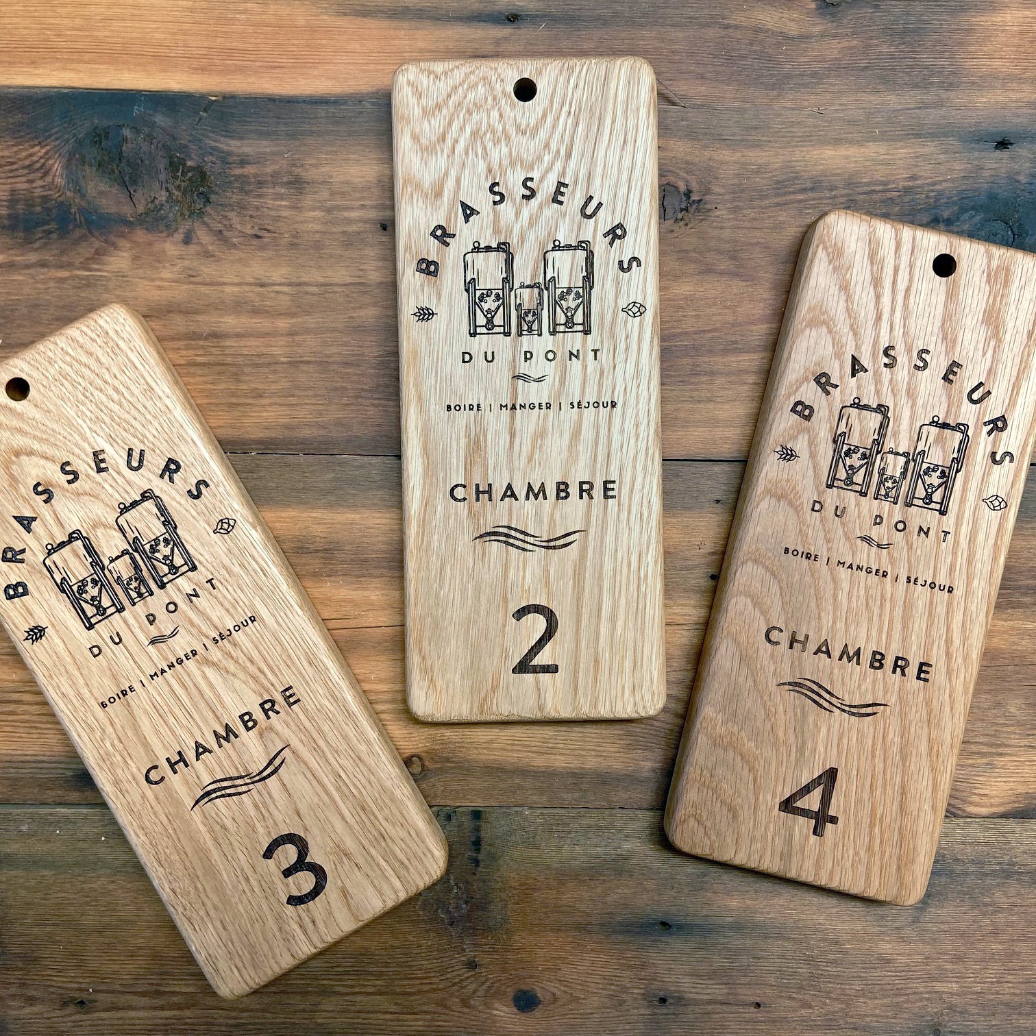 Three Hotel room signs with drill hole at top for hanging. Engraved with Brassuers du Pont Hotel Logo and the room names and numbers. 